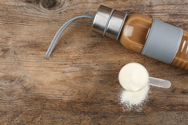 Proteína en polvo con cuchara sobre mesa de madera junto a botella deportiva