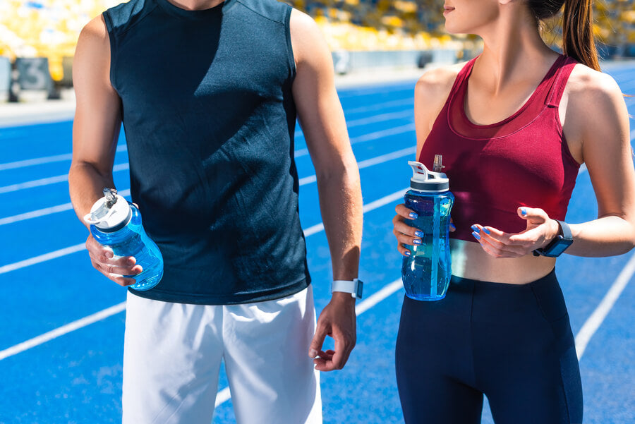 Dos personas deportistas conversando y sosteniendo botellas de agua en una pista azul.