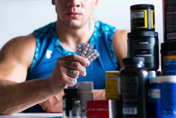 Creatina hcl y monohidratada - Hombre sosteniendo pastillas entre suplementos deportivos.