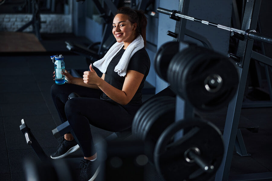 Creatina masticable para que sirve - Mujer sonriendo en el gimnasio con toalla y botella de agua