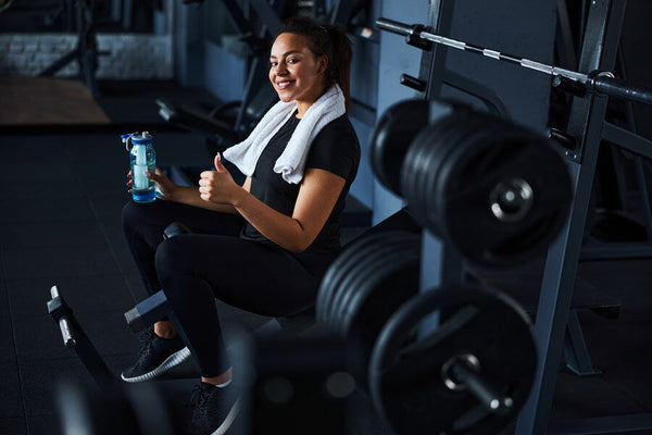 Creatina masticable para que sirve - Mujer sonriendo en el gimnasio con toalla y botella de agua