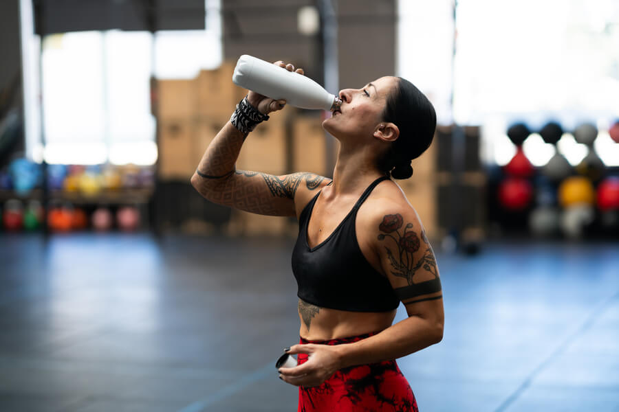 Creatina monohidratada como tomar - Mujer deportista hidratándose con un batido o suplemento en el gimnasio