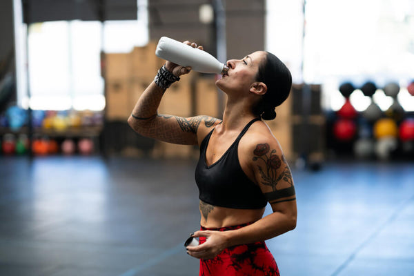 Creatina monohidratada como tomar - Mujer deportista hidratándose con un batido o suplemento en el gimnasio