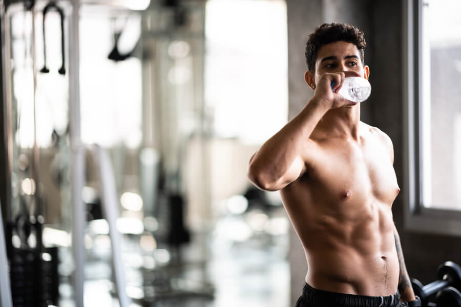Hombre entrenando en el gimnasio mientras bebe agua.