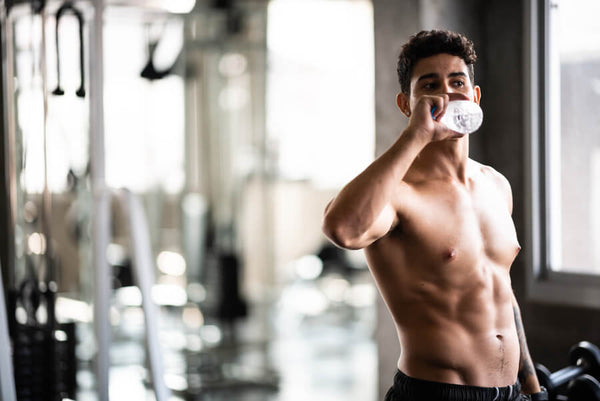 Hombre entrenando en el gimnasio mientras bebe agua.