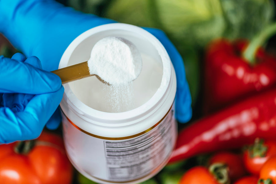Polvo blanco en suplemento alimenticio siendo medido con cuchara sobre fondo de verduras frescas