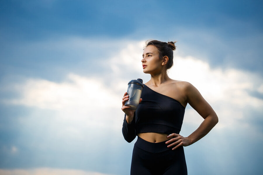 Para que sirve la proteina de carne - Mujer deportista sosteniendo batido proteico al aire libre.