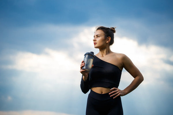 Para que sirve la proteina de carne - Mujer deportista sosteniendo batido proteico al aire libre.