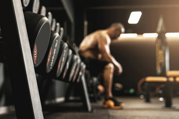 Proteina de carne isolada - Mancuernas en primer plano con atleta descansando en gimnasio.