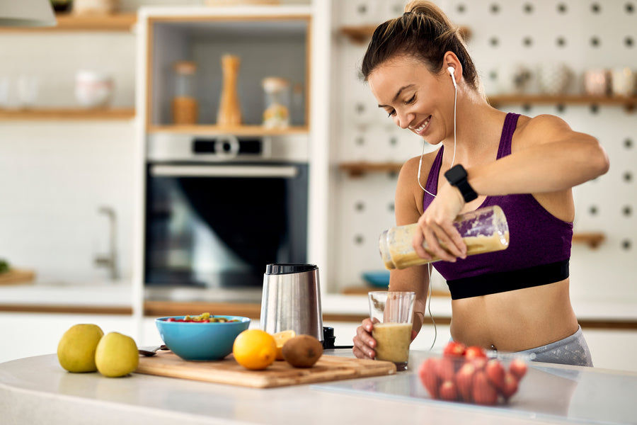 Proteína hipercalórica beneficios - Mujer preparando batido de frutas en la cocina.