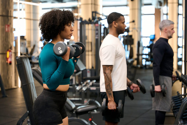Personas entrenando con mancuernas en gimnasio.