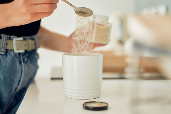 Persona agregando proteína en polvo a un vaso en cocina.