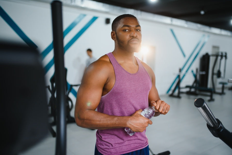 Proteínas whey para que sirve - Hombre deportista en gimnasio sosteniendo una botella de agua.