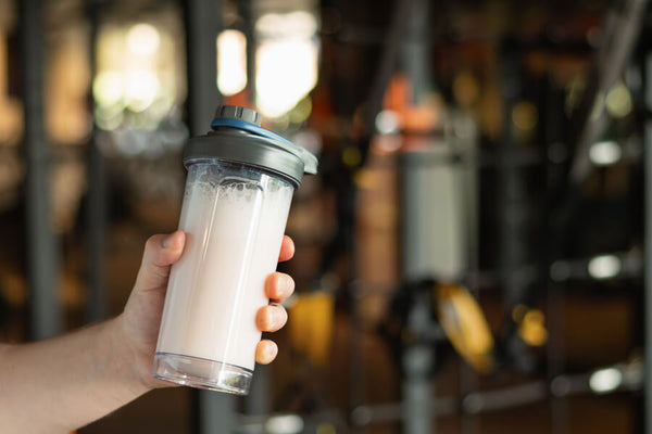 Qué son las proteínas hidrolizadas - Persona sosteniendo un batido de proteína en un gimnasio.